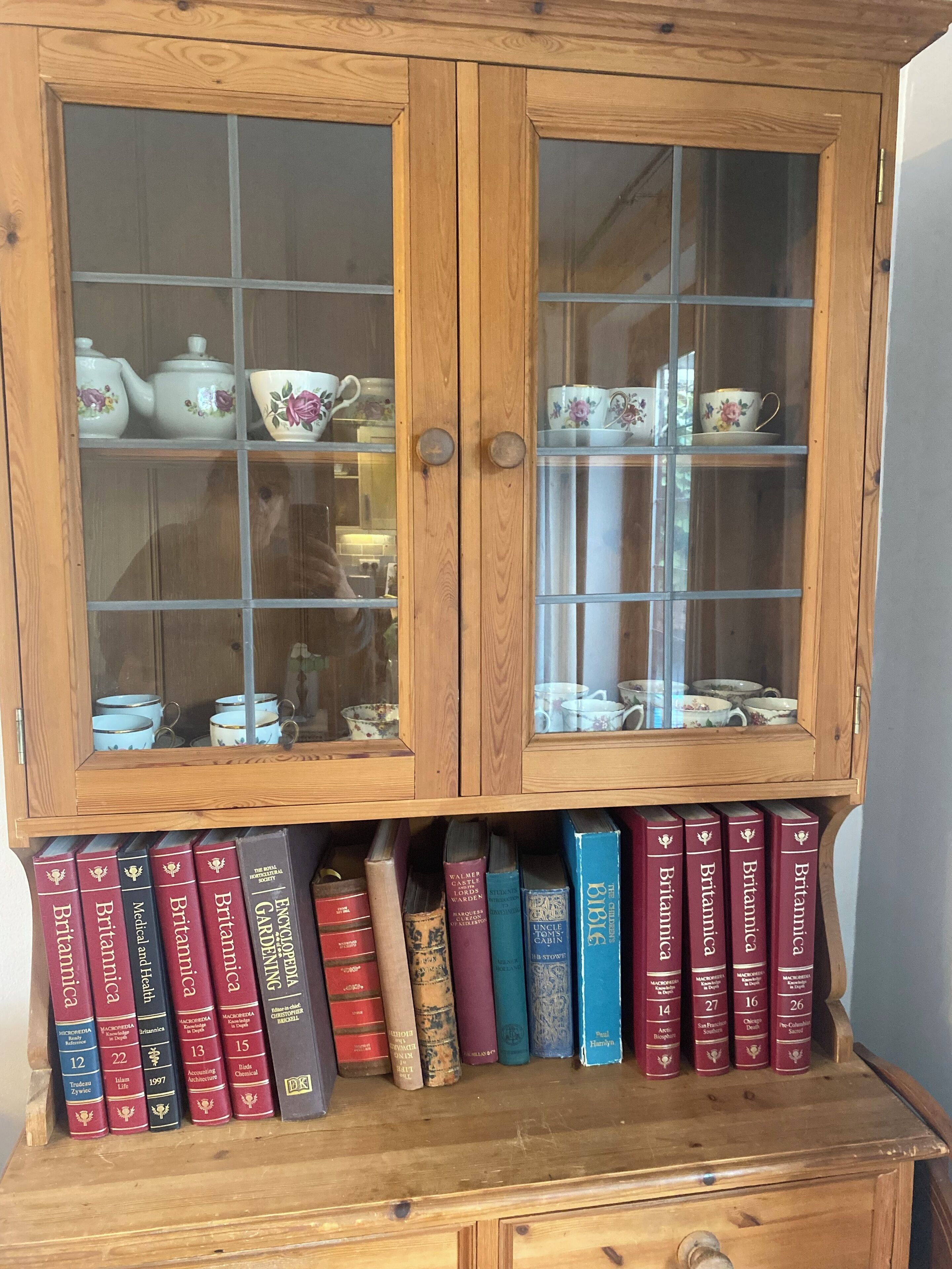 Un gabinete de madera con puertas de cristal, que contiene libros y teteras.