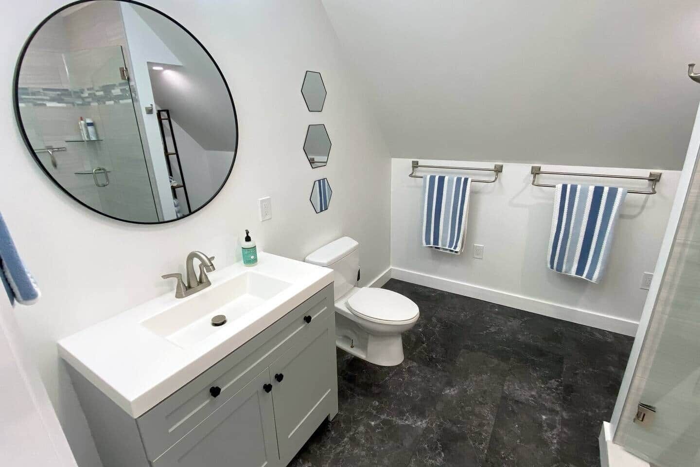 A modern bathroom with a white vanity, a round mirror, a toilet, and a shower area.