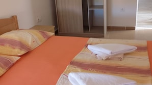 Un dormitorio con dos camas, una colcha naranja, un armario de madera y piso de baldosas.