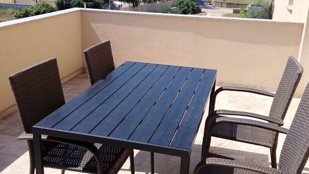Un balcón con una mesa y cuatro sillas de mimbre.