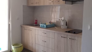 Una cocina con armarios de madera clara, un lavamanos de acero inoxidable, una cafetera y un cubo de basura.