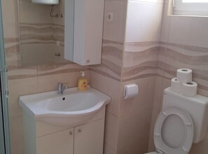 A bathroom with a white sink, a mirror, a soap dispenser, a toilet, and toilet paper. - Apartments Marta (Vrsi)