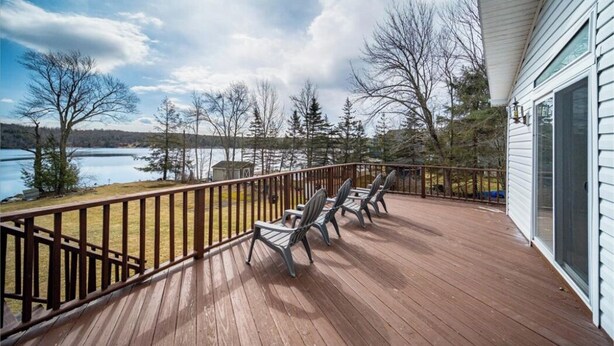 A wooden deck with chairs overlooking a lake, surrounded by trees. - Catskills Lakefront Getaway at Sackett Lake (Monticello)