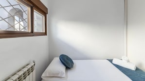 A small, single-bed room with a window, a radiator, a pillow, and a towel.