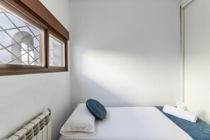 A small, single-bed room with a window, a radiator, a pillow, and a towel.