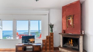 A living room with a TV, fireplace, and large windows overlooking the sea.