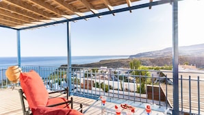 A balcony with a view of the sea, a table with drinks, and a red chair.