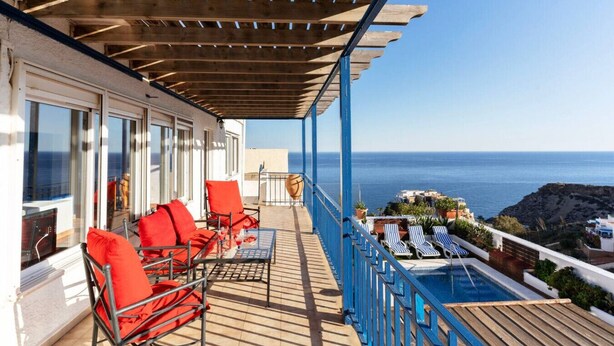 A balcony with red chairs, a pool, and a view of the sea.