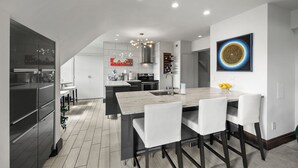Una cucina moderna con isola centrale, sgabelli da bar bianchi e un'ampia finestra.
