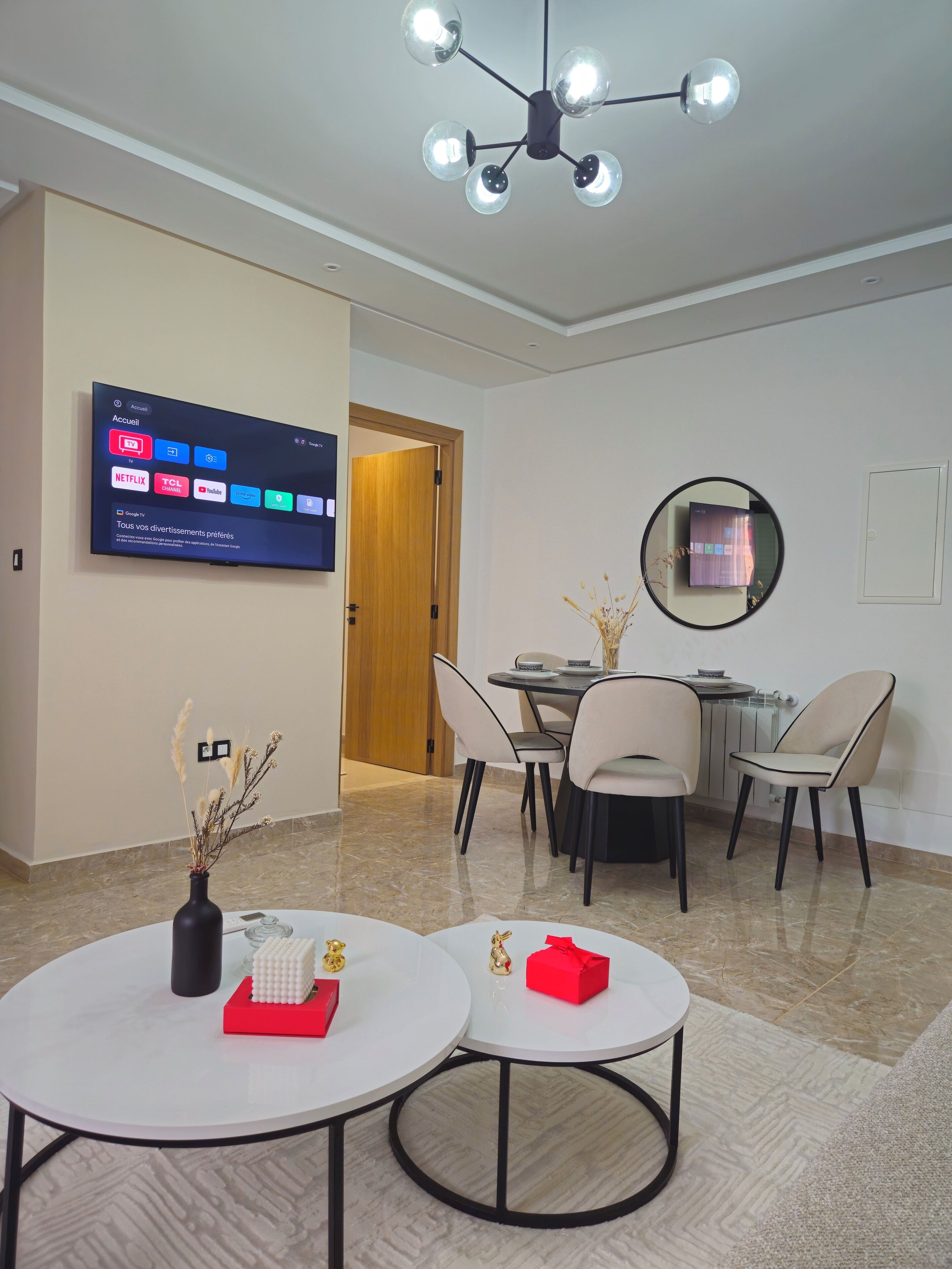 Un soggiorno moderno con una TV a schermo piatto che mostra servizi di streaming, una zona pranzo con un tavolo rotondo e sedie, e un vaso decorativo su un tavolino.