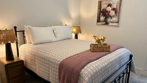 Un lit bien fait, recouvert d’une couvre-lit à motifs, avec deux lampes de chevet, une petite table de chevet et un vase décoratif posé sur le lit.