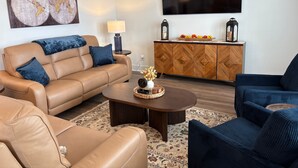 Un salon comprenant un canapé, un fauteuil, une table basse et un téléviseur fixé au mur.