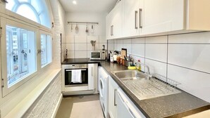Een moderne keuken met witte kasten, een inbouwoven, een magnetron en een spoelbak met afwassrek.