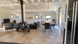 A spacious living area with a fireplace, a dining table, and a kitchen in the background.