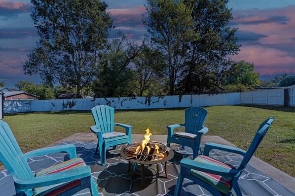 An outdoor seating area with four blue Adirondack chairs around a fire pit.