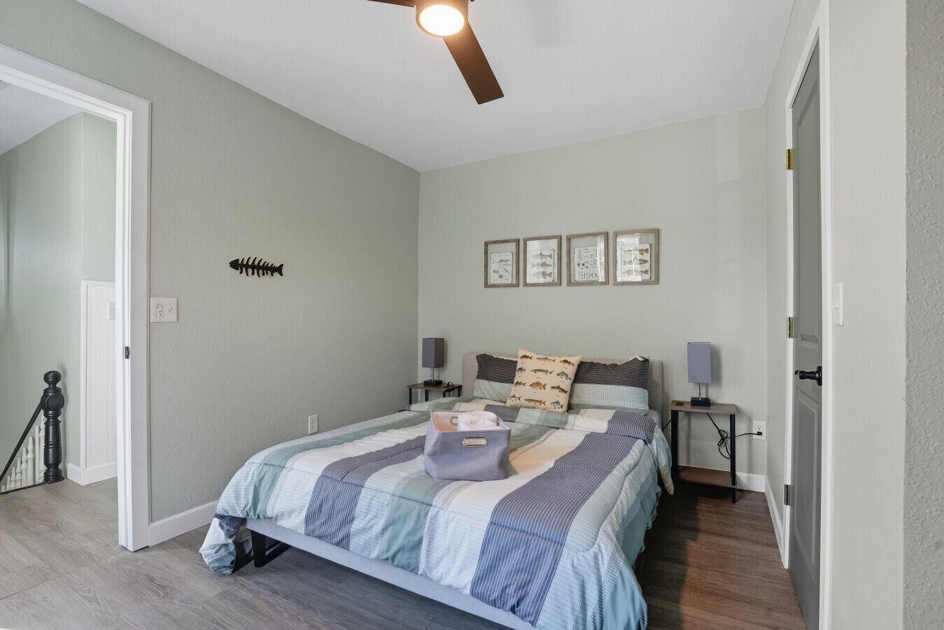 A bedroom with a bed, a ceiling fan, a fish wall art, framed pictures, and a door.