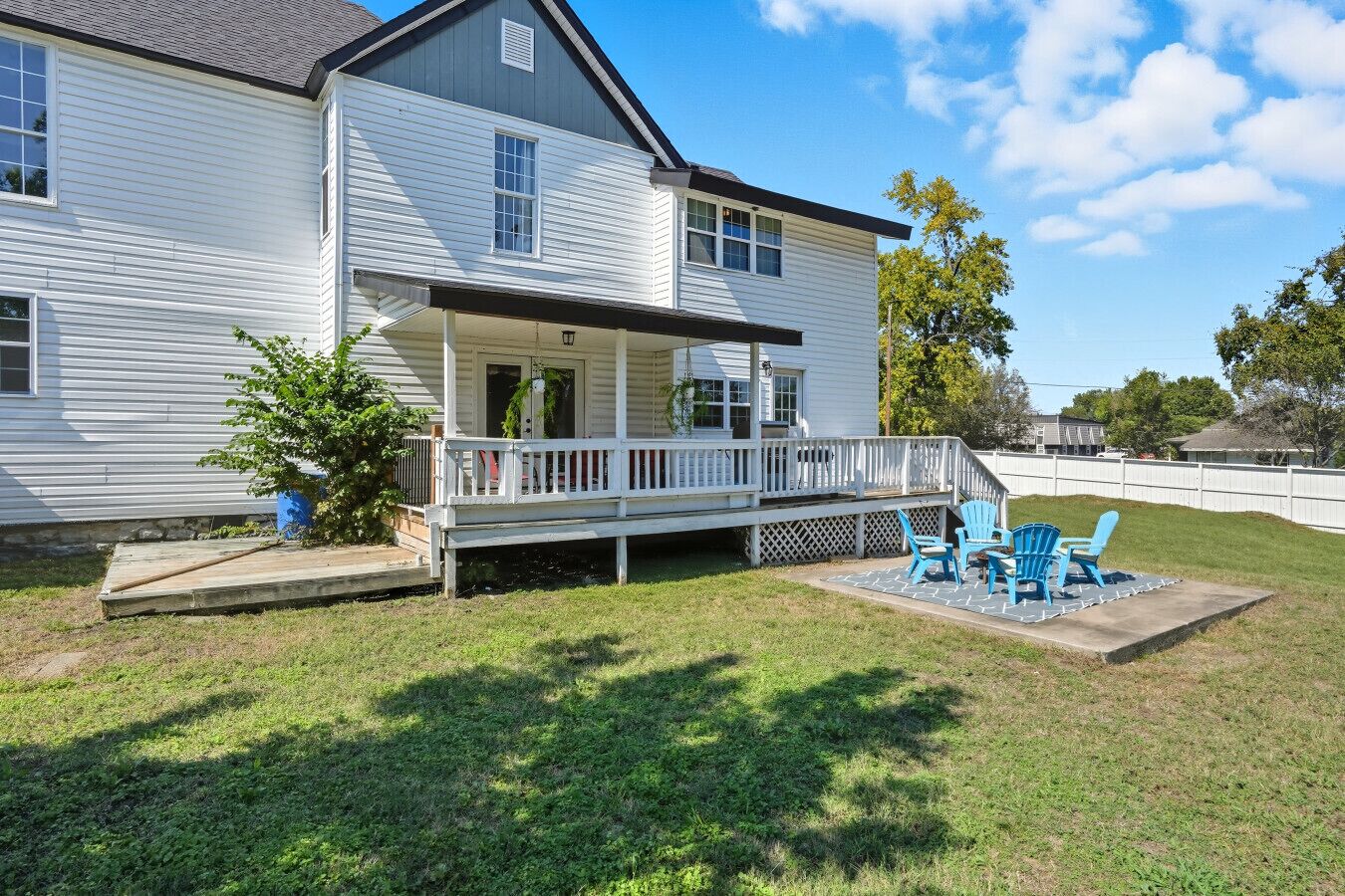 A two-story house with a covered porch and a small patio area with blue chairs.