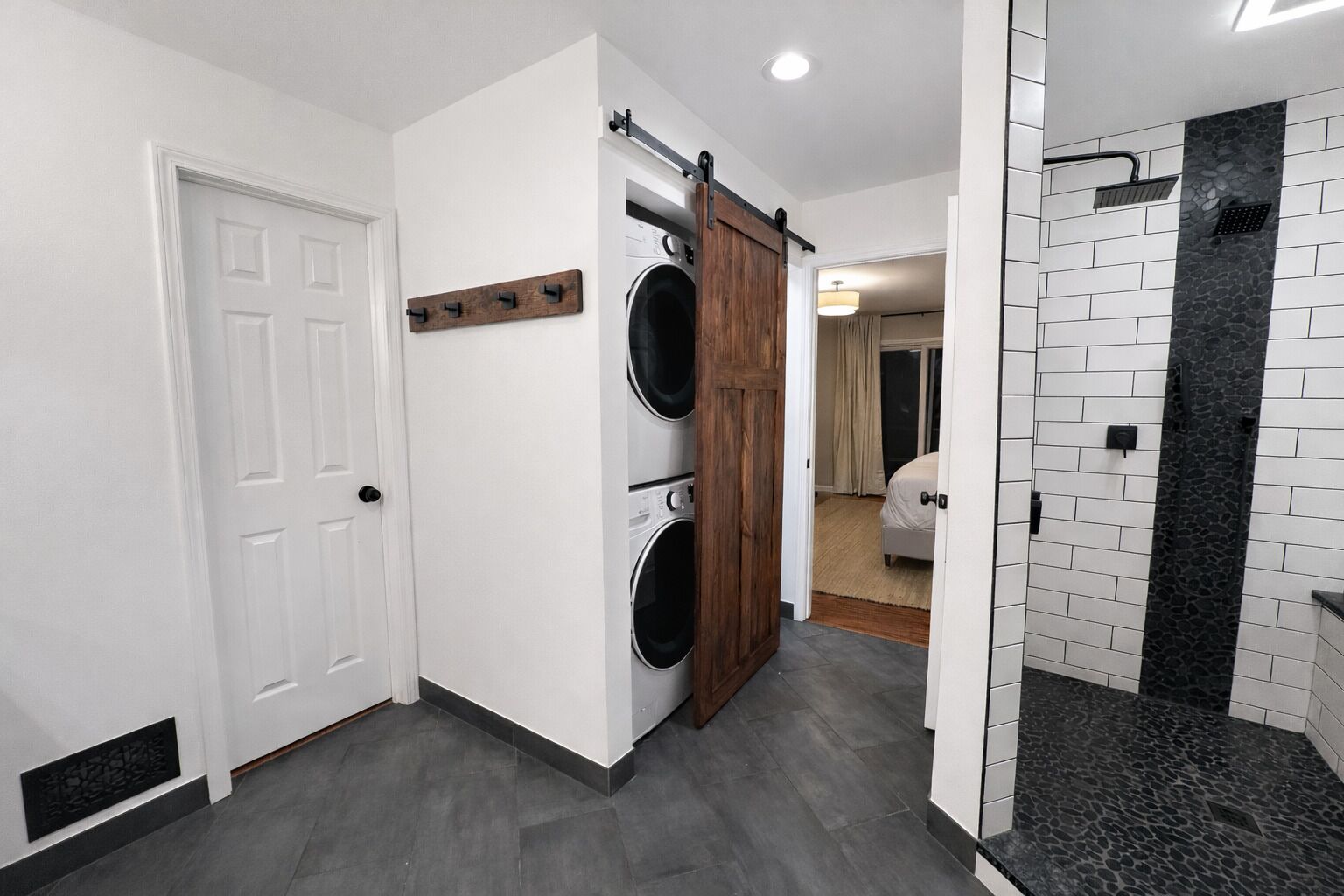 A hallway with a white door, a wooden sliding door, and a shower area with black tiles.
