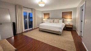 A bedroom with a large bed, two bedside tables, a ceiling light, a sliding glass door, and a view of the outdoors. - All-Sports Lakefront Retreat w/ Private Beach, Dock & Tiki Bar - Sleeps 10 (Linden)
