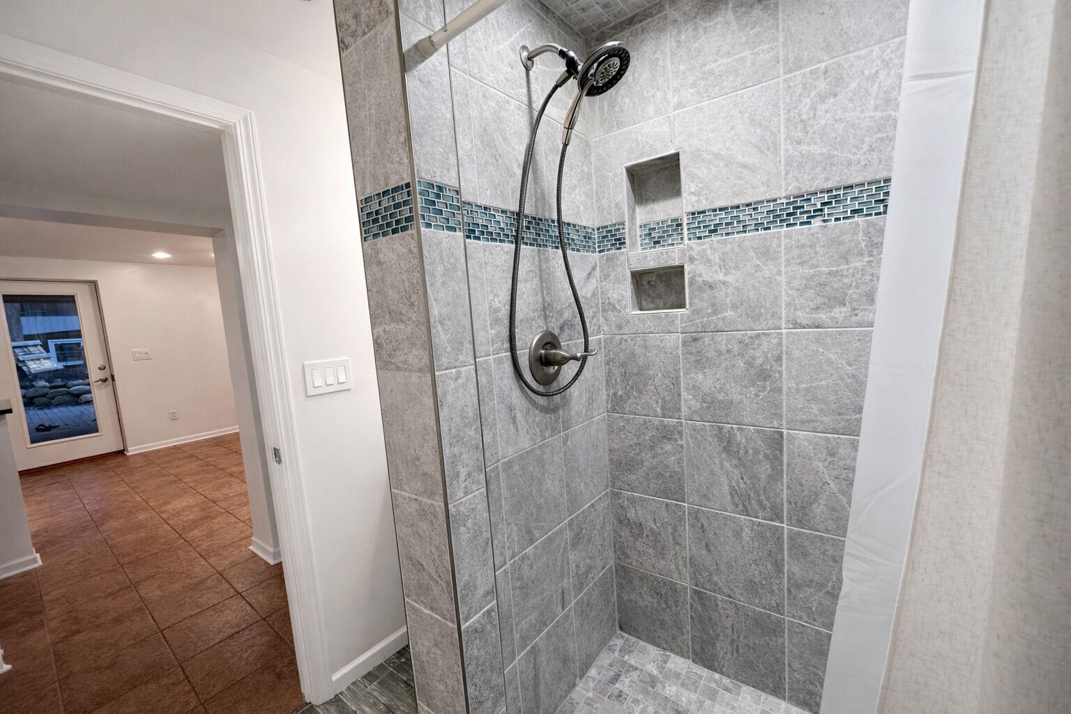 A shower area with a glass door, tiled walls, and a small shelf.