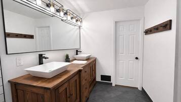 A bathroom with a large mirror, two sinks, wooden cabinets, a potted plant, and a white door.
