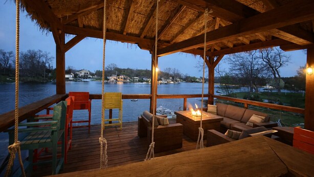 A wooden deck with a thatched roof, outdoor seating, and a fire pit. - All-Sports Lakefront Retreat w/ Private Beach, Dock & Tiki Bar - Sleeps 10 (Linden)