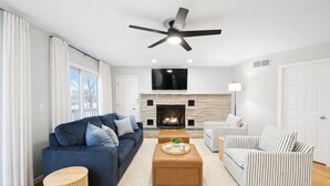 A modern living room with a fireplace, a sofa, a striped armchair, and a coffee table. - All-Sports Lakefront Retreat w/ Private Beach, Dock & Tiki Bar - Sleeps 10 (Linden)