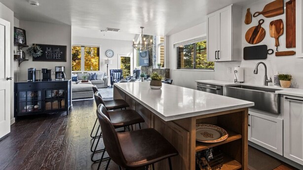 Una cucina moderna con una grande isola, sgabelli da bar, forno integrato e una varietà di utensili di legno appesi al muro.