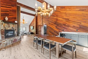 A spacious dining area with a wooden table and chairs, a stone fireplace, and a modern chandelier.
