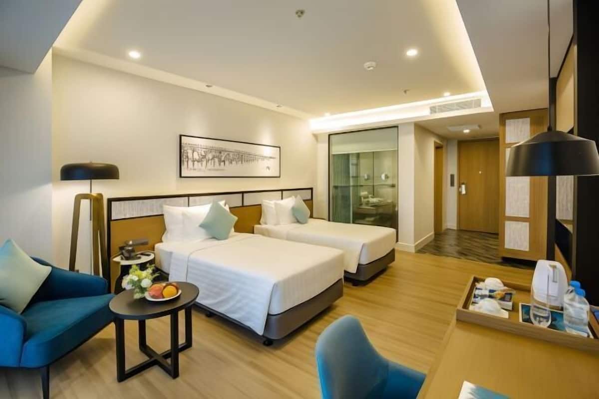 A hotel room with two beds, a sofa, a small table with a fruit bowl, and a tray with toiletries.