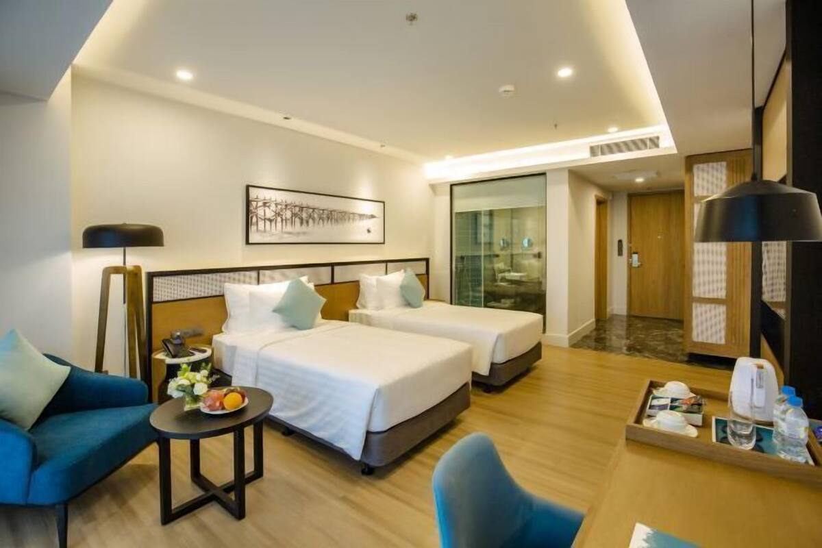 A hotel room with two beds, a sofa, a small table with a tray of items, and a large window.