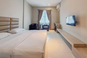 A hotel room with a large bed, a TV mounted on the wall, a desk, and a chair. - Nagoya One Hotel (Batu Ampar)