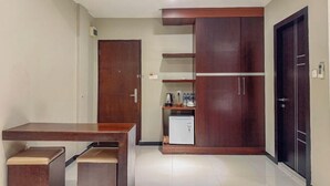 A compact kitchen with a wooden table and cabinets, a small refrigerator, and a door. - Nagoya One Hotel (Batu Ampar)
