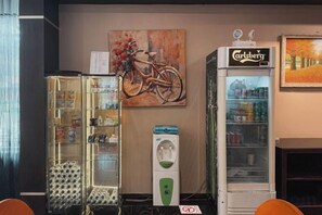 A room with a glass display cabinet, a refrigerator, and a painting of a bicycle. - Nagoya One Hotel (Batu Ampar)