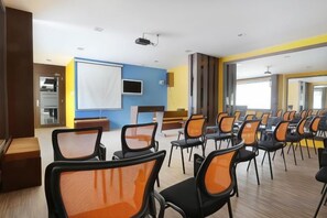 A conference room with rows of chairs, a projector, and a large screen. - Nagoya One Hotel (Batu Ampar)