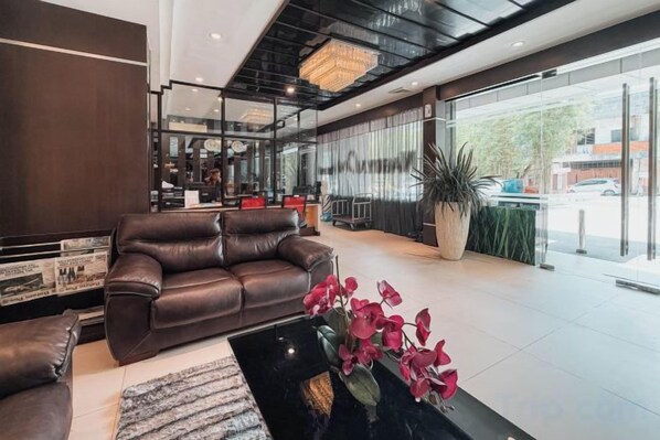 A modern lobby with a leather sofa, a coffee table with flowers, and a large window offering a view of the street. - Nagoya One Hotel (Batu Ampar)