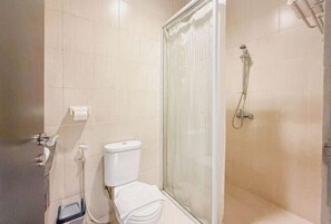 A bathroom with a toilet, a shower with a glass door, and a towel rack. - Nagoya One Hotel (Batu Ampar)