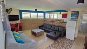 A living room with a sofa, a coffee table, a TV, and a kitchen area with a refrigerator and a sink. - La Villa verte (Robert)