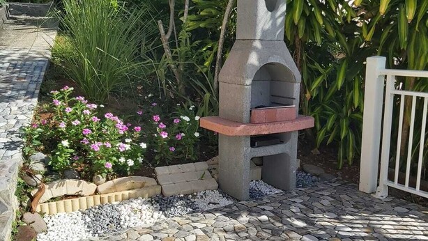 A stone oven structure surrounded by a garden with various plants and a stone-tiled pathway. - La Villa verte (Robert)