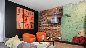 A modern living room with a brick wall, two orange armchairs, a grey sofa, and a small table with drinks. - Stable #5 ~ Mini Golf, Fire Pits, Games, Walkable (Louisville)