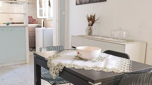 A dining area with a table set for four, a white vase with dried plants on a white console table, and a painting of red flowers on the wall. - The Ideal Shelter for Families "Discover the heart of Mesagne (Mesagne)