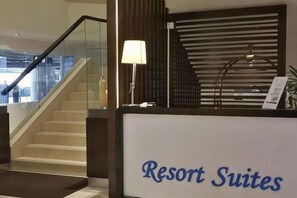 Un mostrador de recepción con un letrero que dice 'Resort Suites' y una escalera que sube a pisos superiores.