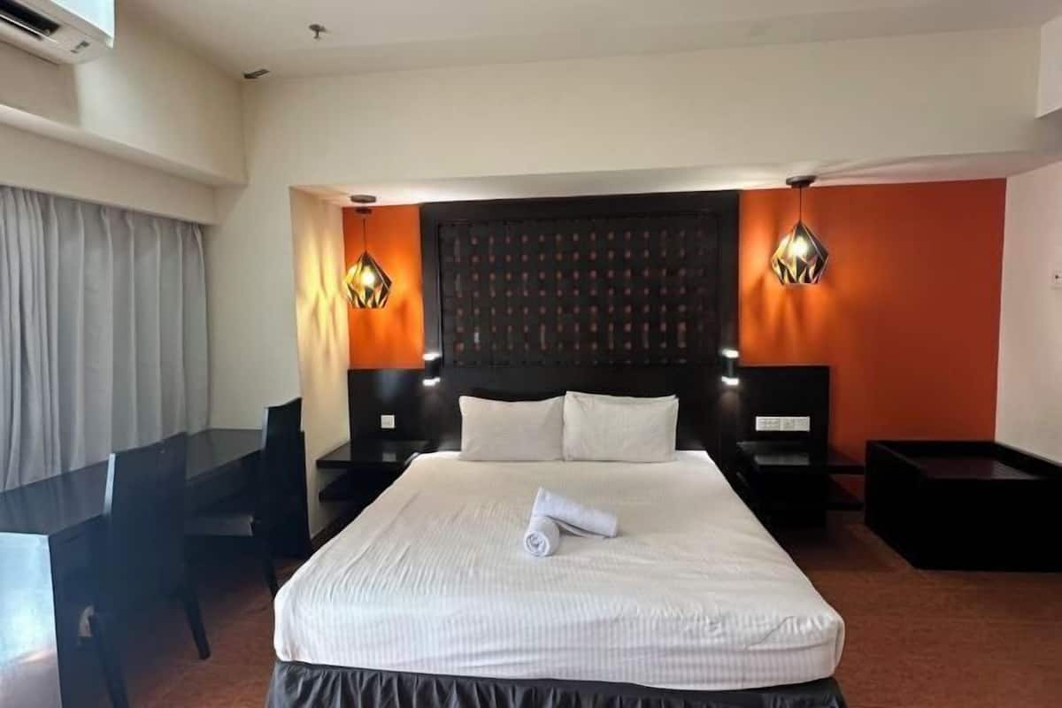 Habitación de hotel con una cama grande, un escritorio, dos mesitas de noche y un cabecero con diseño estampado.