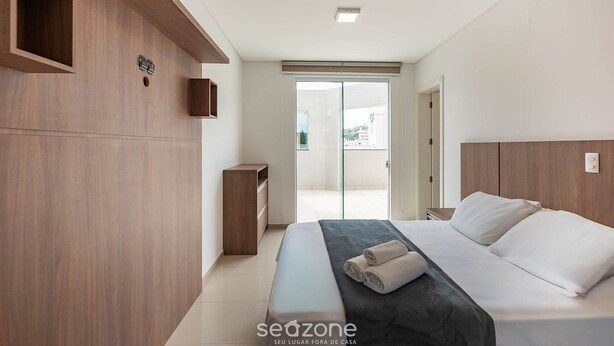 A modern bedroom with a large bed, wooden paneling, a small bedside table, and a sliding glass door leading to a balcony. - Apt. w/ Balcony and BBQ 250m From the sea Mrs0402 (Bombinhas)