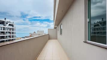 Un balcón estrecho con suelo de baldosas, vistas al mar y edificios colindantes.