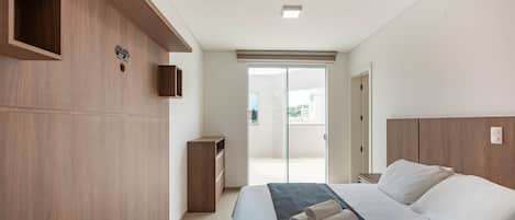 Un dormitorio moderno con una cama grande, paneles de madera, una mesita de noche pequeña y una puerta corrediza de vidrio que da a un balcón.