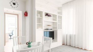 Een lichte, witte kamer met een eettafel, stoelen, een televisie en inbouwkasten.