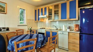 A compact kitchen with wooden cabinets, a blue refrigerator, and a dining table set for four. - Holiday Home Brsec-Two Bedroom Holiday Home with Sea View (Brsec)