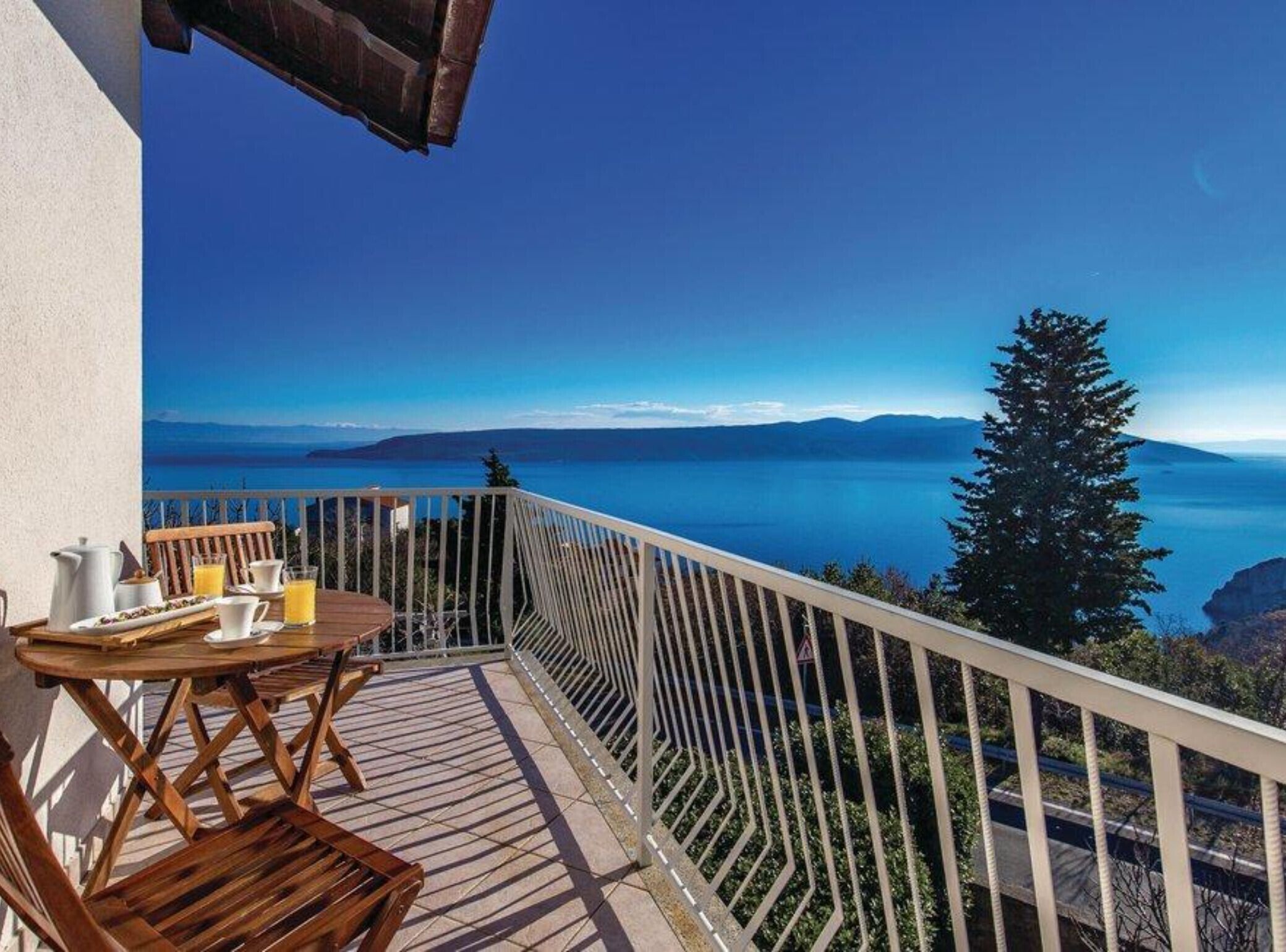 Un balcon avec une table dressée pour le petit-déjeuner, offrant une vue panoramique sur un plan d’eau et des montagnes lointaines.