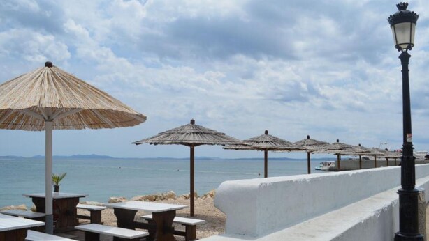 A beachside patio with wooden tables and thatched umbrellas, overlooking the sea. - Apartments Matković - Two Bedroom Apartment1 (Vir)